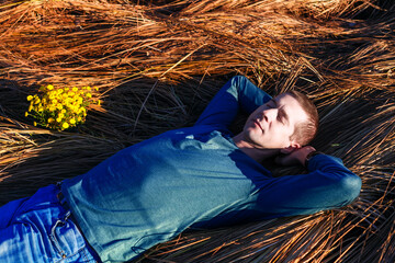 resting calm man lies on dry grass, dreams, closed his eyes, put his hands under his head. Dressed...