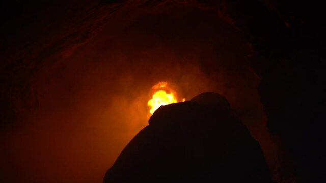 Silhouette of a young man exploring a cave filled with smoke with his selfmade torch