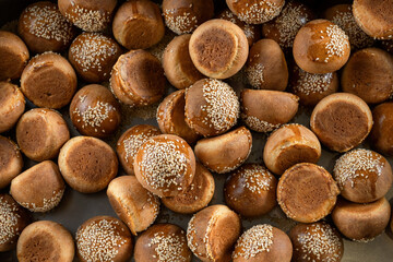 The homemade bread rolls with sesame. Lots of rolls are poured onto the baking sheet.