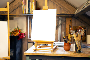 Artistic equipment in a artist studio: empty artist canvas on wooden easel and paint brushes Retro toned photo copy space