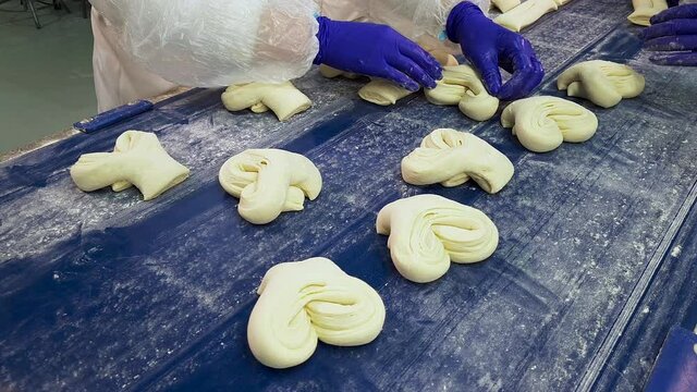 Group of women workers making delicious sweet buns of dought on a moving conveyor belt. Modern automated bakery. Food production industry.