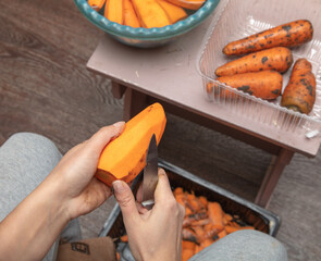 A woman peels a carrot with a knife.