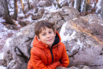 Naklejka na ściany i meble Portrait of a boy (8 years old, white, Caucasian) near a large stone in the mountains in winter in the bright sun