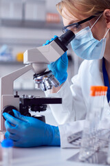 Close Up Of Female Lab Worker Wearing PPE And Safety Glasses Looking At Slide Under Microscope