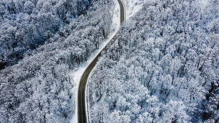 Top view of empty road along winter forest after snowfall. Aerial view of winding road through trees covered with snow