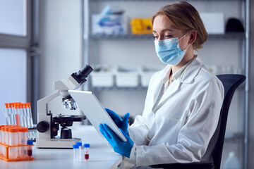 Female Lab Worker Wearing Lab Coat Working On Covid-19 Vaccine With Digital Tablet And Microscope