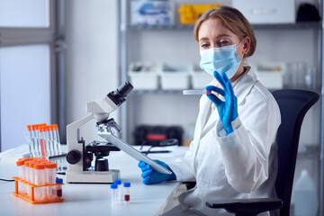 Female Lab Worker Wearing Lab Coat Working On Covid-19 Vaccine With Digital Tablet And Microscope