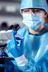 Close Up Of Female Lab Worker Wearing PPE Researching Omicron Variant Of Covid-19 With Microscope