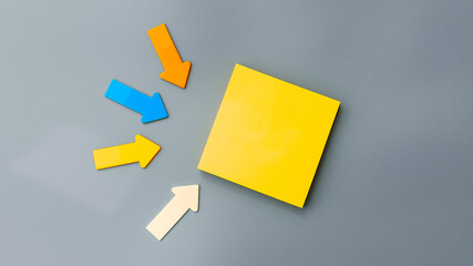 blank yellow square sticky note and colorful arrows of paper on gray background, top view. Blank...