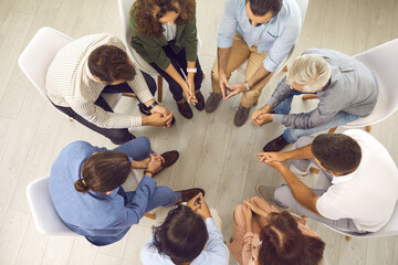 Overhead view of young and mature patients meeting for conversation with psychologist or psychotherapist. High angle shot of group of people sitting in circle during therapy session with psychiatrist