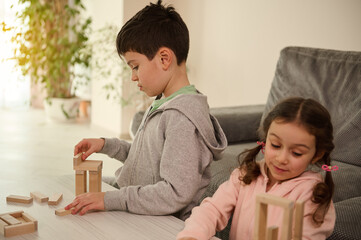Development of fine motors skills and concentration, educational leisure, family pastime concept. Focused children building structures with wooden blocks, playing board games in the home living room.