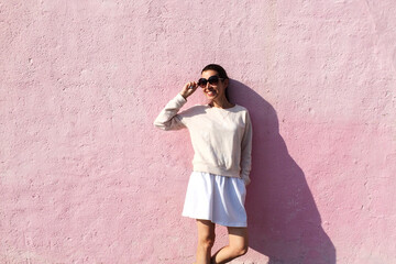 Woman in sunglasses standing near pink wall on sunny summer day