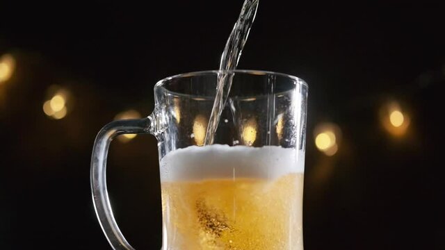 Pouring Fresh Frothy Draft Beer into a Glass at a Bar or Pub over Dark Background, Slow Motion