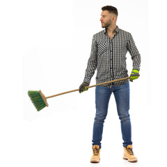 Handsome young man is standing with broom and looking to the side. Full length, isolated.