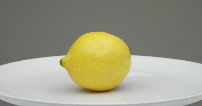 Fresh ripe yellow Lemon on a while plate spinning. Close up studio shot, isolated on gray background, real time, no people