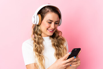 Young brazilian woman isolated on pink background listening music and looking to mobile