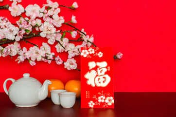 Red envelope packet or ang bao(word mean wealth, sentence mean may all go well, great fortune and profit) puts with tea set and oranges that have peach blossom on red glitter paper background.