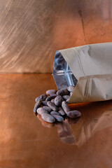 Dried cocoa beans are poured on a copper surface from a hermetic paper bag. Copy space. Vertical image. 
