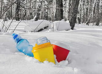 Multi-colored coffee cups, a plastic bottle and a glass jar stick out of the snow in a winter...