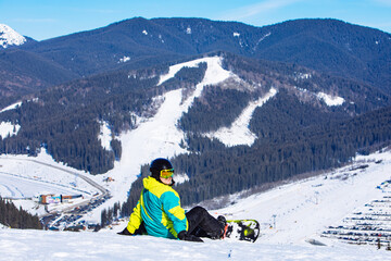 man sitting with snowboard on the top of the hill with beautiful view