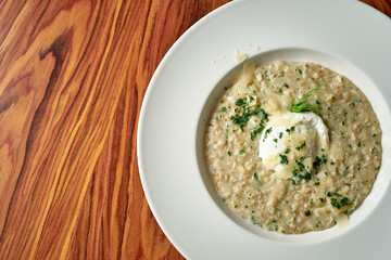 Oatmeal with parmesan and poached egg in a white plate on a wooden background