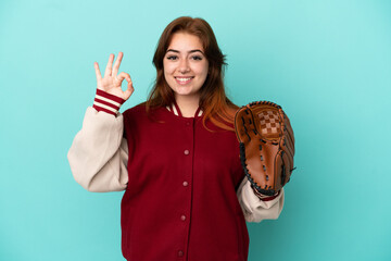 Young redhead woman playing baseball isolated on blue background showing ok sign with fingers