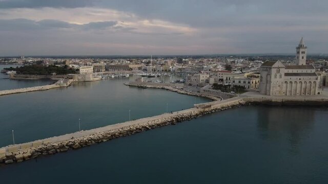 Travelling aereo con drone sulla citt&agrave; Trani, discesa dal cielo verso il mare adriatico mediterraneo di puglia con panoramica da cattedrale e campanile verso il porto e centro storico