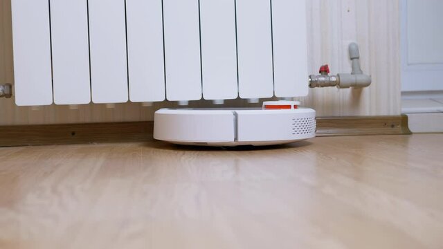 A Modern Automatic Robot Vacuum Cleaner Sweeps Debris on Floor in Room. A rotation white vacuum cleaner with small brushes, touch motion sensor. Autonomous room cleaning. Smart home assistant. 4K.