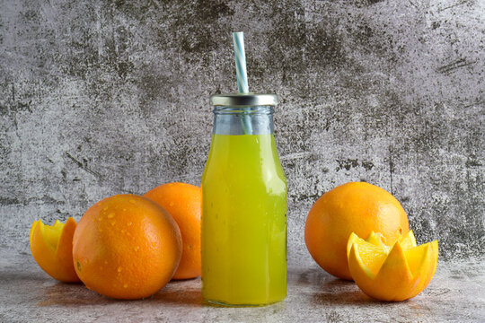Refreshing orange in glass bottle with cane. Stone background with scattered oranges.