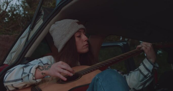 Young woman on the road playing acoustic guitar cold evening