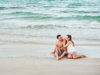 Fototapeta premium Handsome man and pretty woman sitting on the beach with the sea background and looking into the distance. Outdoors, closeup. Concept of leisure and travel
