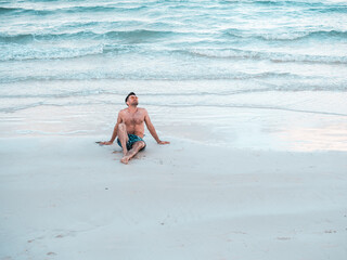Handsome man on the beach against the background of the sea, looking into the distance. Outdoors, closeup. Concept of leisure and travel