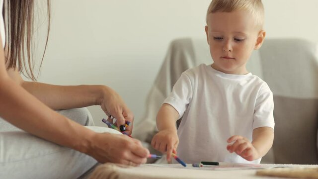 European family mom and son draw with pencils and read a book at home. single mother brings up a child, teaches him to draw, read and play, a beautiful woman and a cute boy have fun in their cozy home