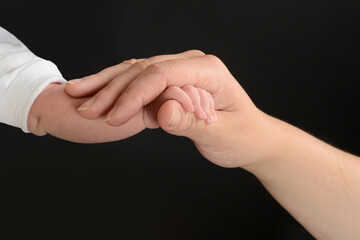 Small hand of a newborn baby held by the hand of its mother where the difference of skins can be appreciated.