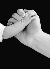 Fototapeta premium Hand of an adult person holding the little hand of a baby isolated on black background.