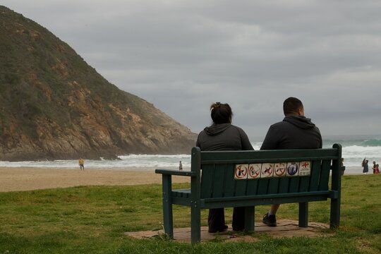 Two people sitting on a bench looking out accross a sea view at Herolds Bay in the Western Cape Province of South Africa.