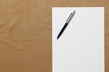 Template of white paper with pen lies on light brown cloth background. Concept of business plan and strategy. Stock photo with empty space for text and design.