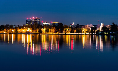 Fototapeta premium Night view of the colorful reflection of city lights in the lake's water from the Herastrau park. Bucharest, Romania.