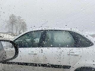 view of the white car from the car window through the falling raindrops in the parking lot on a cloudy day, bad weather