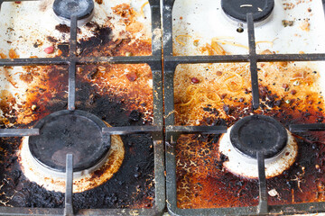 Dirty gas stove surface. Two gas burners and cast iron grate of a gas oven surrounded by old leftovers of food and drinks. Top area surface and burner heads needs cleaning from burnt-on grease 