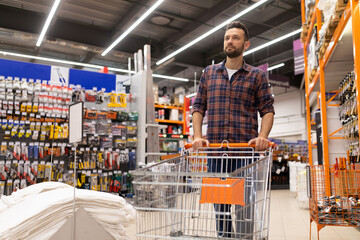 a buyer at a hardware store with a trolley inspects the rows with goods of building materials and...