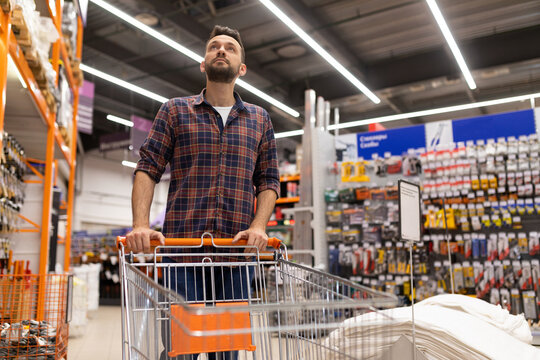 male shopper with a trolley oops examines racks with tools in a construction hypermarket