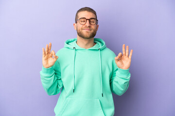 Fototapeta premium Young handsome caucasian man isolated on purple background in zen pose
