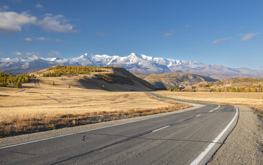 The highway is winding in a mountain valley against the backdrop of mountains and a bright blue sky. Altai, Russia.