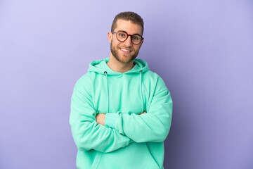 Fototapeta premium Young handsome caucasian man isolated on purple background with arms crossed and looking forward