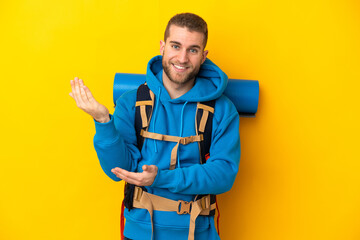 Young caucasian mountaineer man with a big backpack isolated on yellow background extending hands to the side for inviting to come
