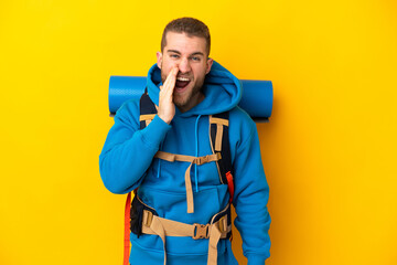 Young caucasian mountaineer man with a big backpack isolated on yellow background shouting with mouth wide open