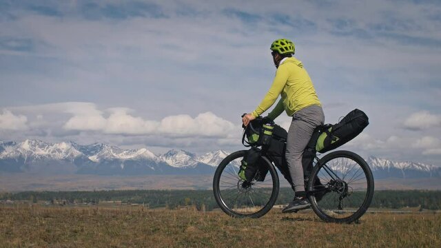 Man stops riding bicycle along field against old mountains