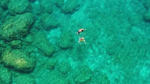Aerial view of a young couple snorkeling above coral reef reaching deeper parts of the crystal clear water, Rhodes, Greece. Aerial drone view of a couple snorkeling swimming in crystal clear water.