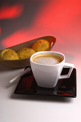 Coffee with milk served in cup with cheese buns on yellow and red colored background.